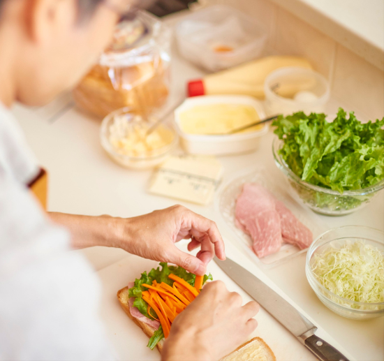 A person preparing a fresh sandwich with lettuce, carrots, and sliced meat in a bright kitchen, symbolising NDIS meal preparation support with Ywecare.