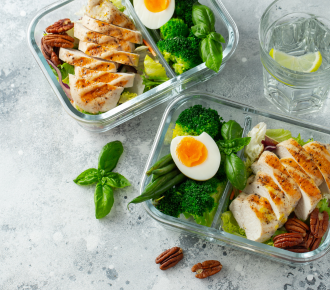 Two healthy meal prep containers with grilled chicken, eggs, broccoli, and nuts, representing NDIS meal preparation support by YWECARE.